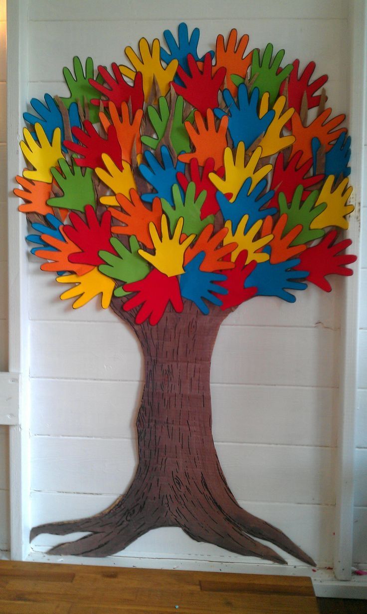 a tree made out of colored handprints on a white wall with wood flooring