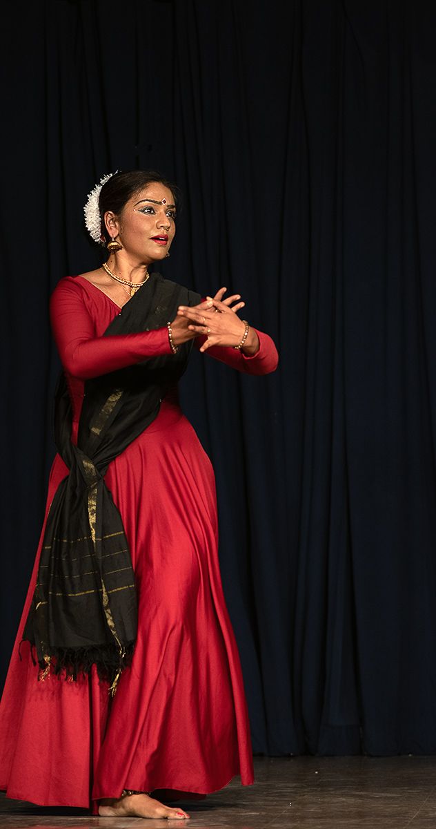 a woman in a red dress standing on a stage with her arms crossed and hands folded