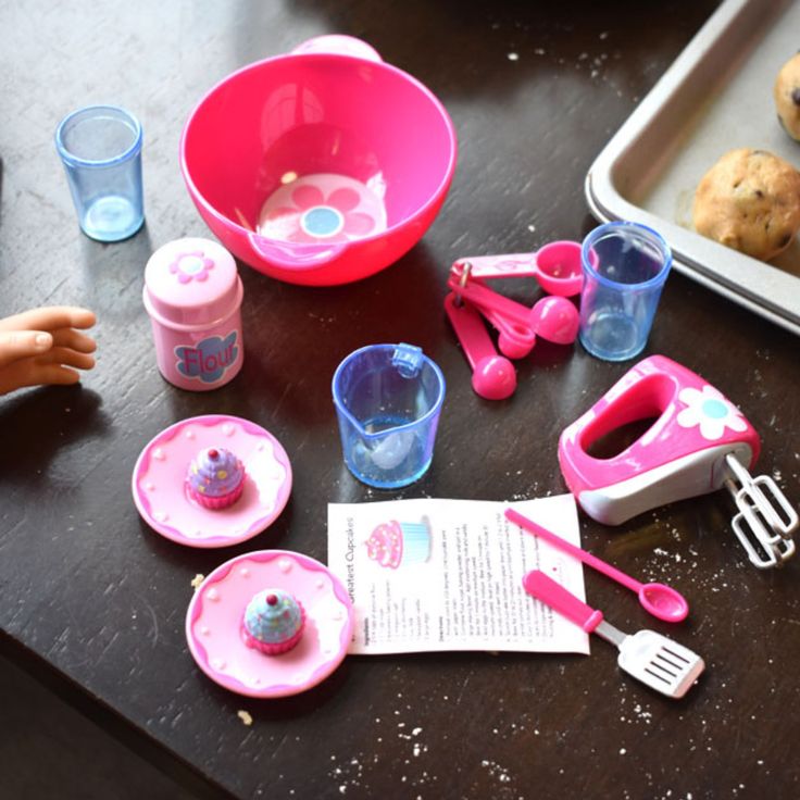 toys and utensils are sitting on a table next to a cookie sheet, cupcake cutters, and baking pan