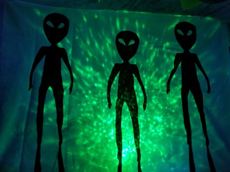 three alien silhouettes in front of a green light