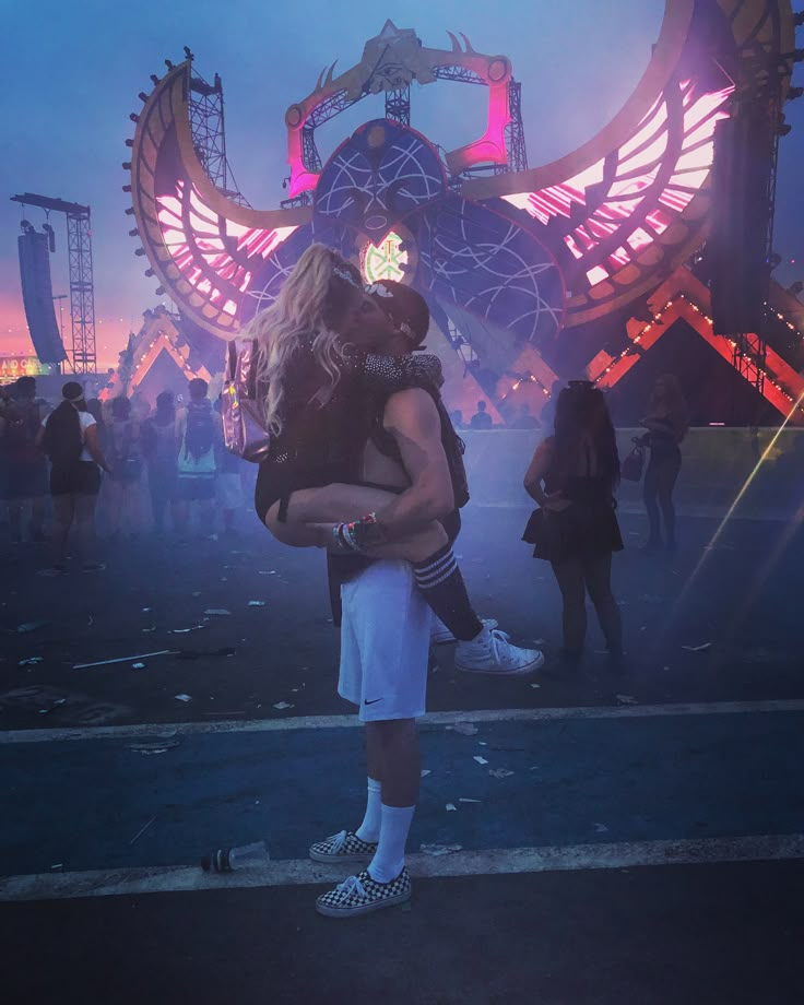 a man and woman hug in front of a stage with lights on it at night