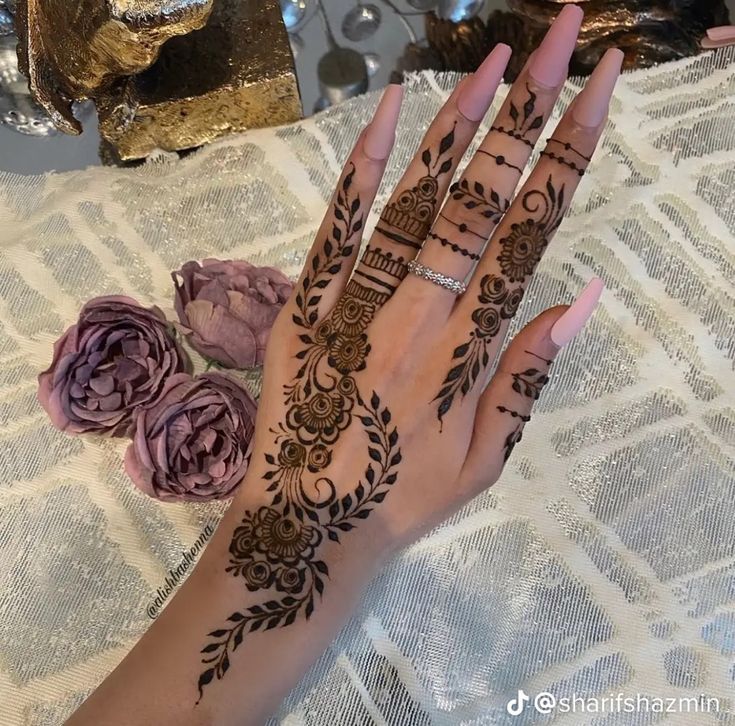 a woman's hand with henna tattoos on it and flowers in the background