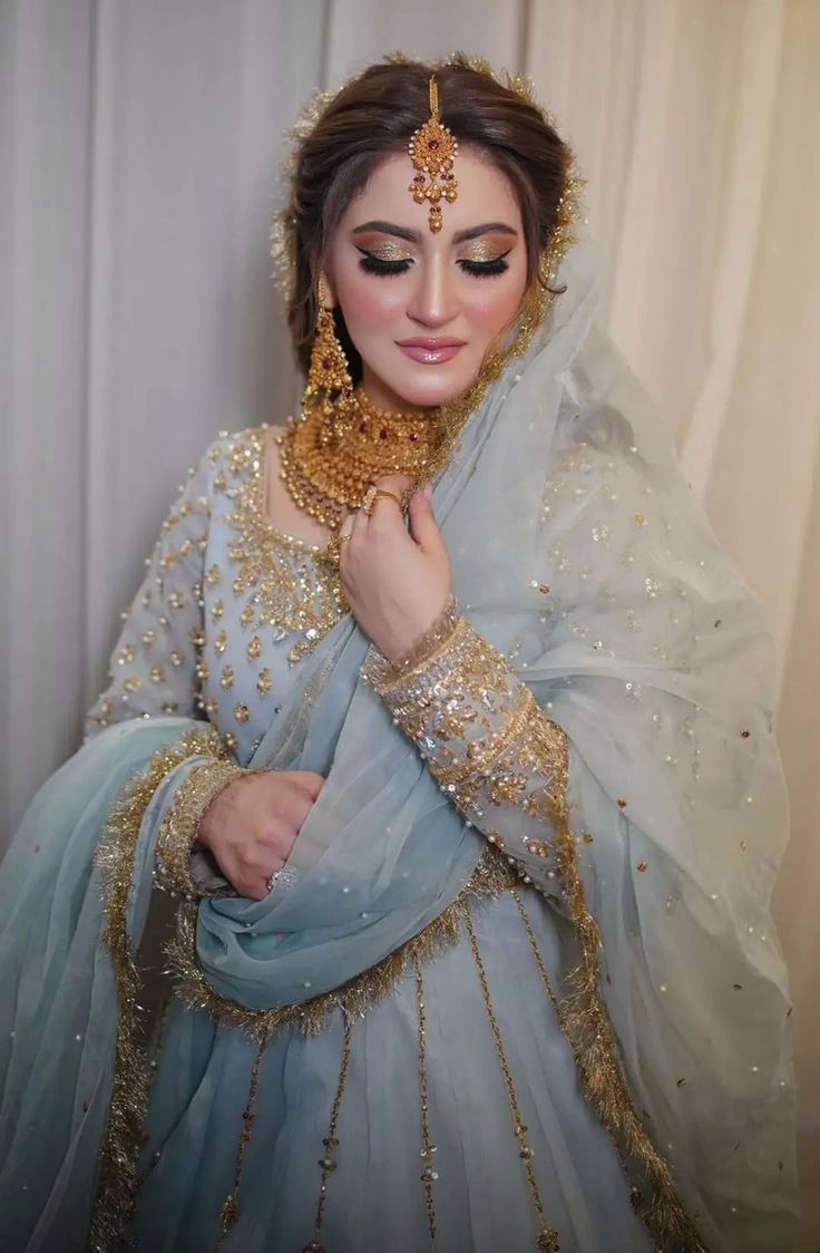 a woman wearing a blue and gold bridal outfit with her hands on her chest