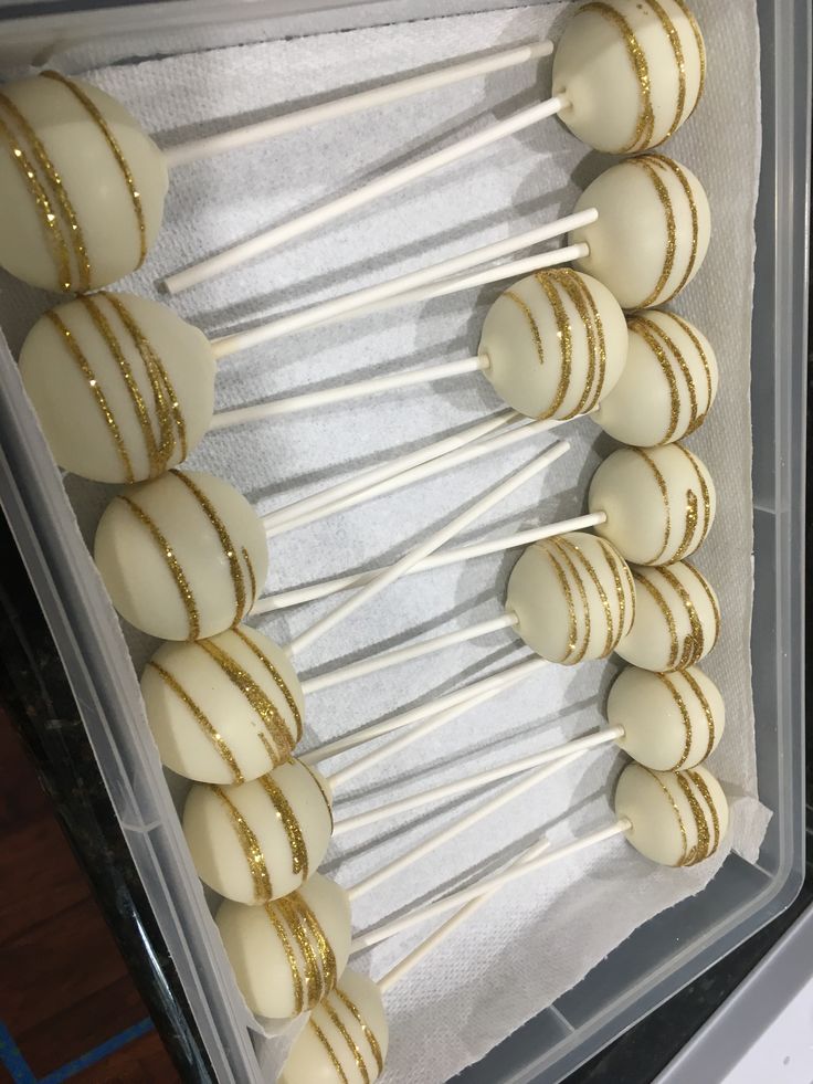 cake pops are lined up in a box with white and gold striped frosting on them