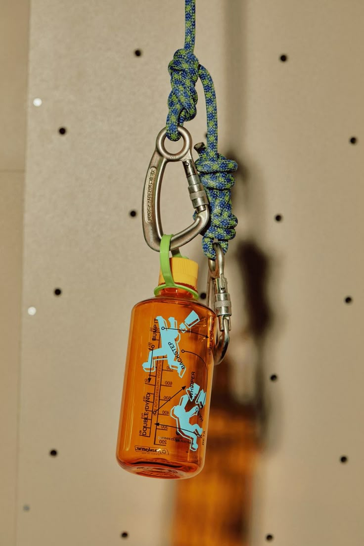 an orange bottle hanging from a hook on a string with a blue and yellow lanyard