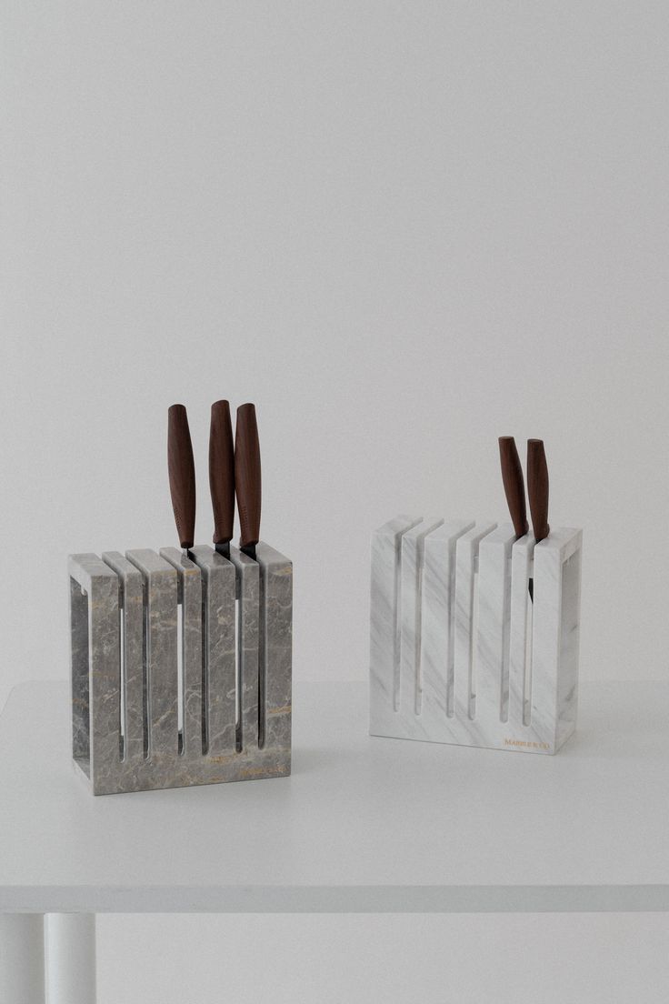 two marble block sculptures with knives sticking out of them on a white table in front of a white wall