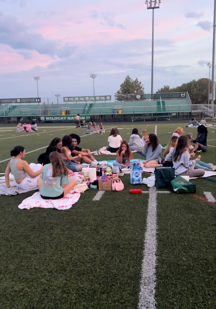 a group of people sitting on top of a field next to each other near a soccer field