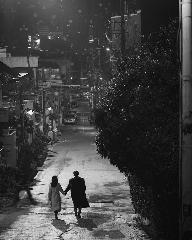 black and white photograph of two people walking down an alley way at night holding hands