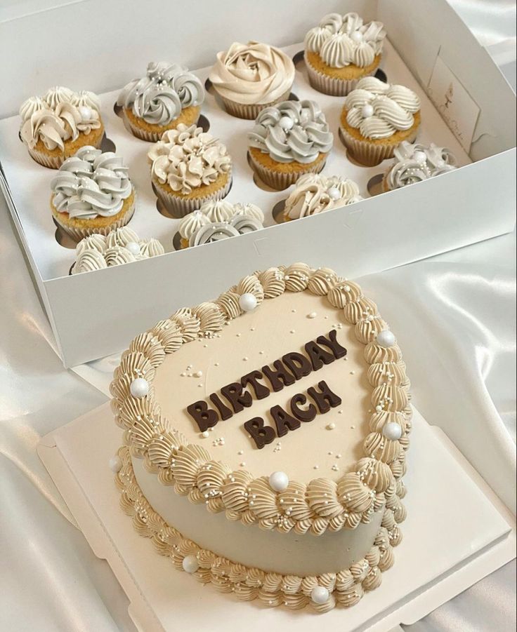 a birthday cake sitting on top of a white box filled with frosting cupcakes