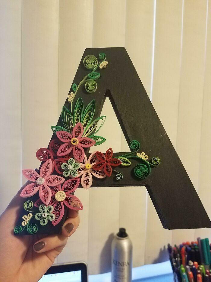 a hand holding up a letter made out of paper flowers and buttons in front of a computer