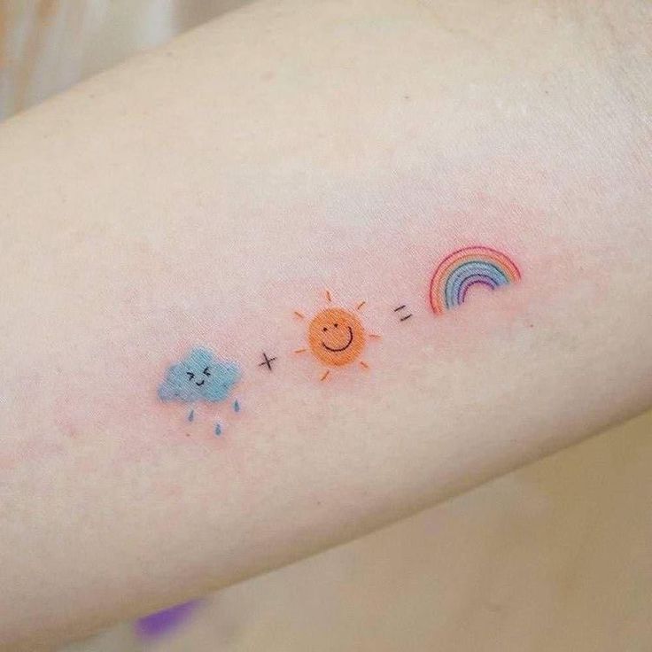 a small sun, cloud and rainbow tattoo on the left arm by someone's hand