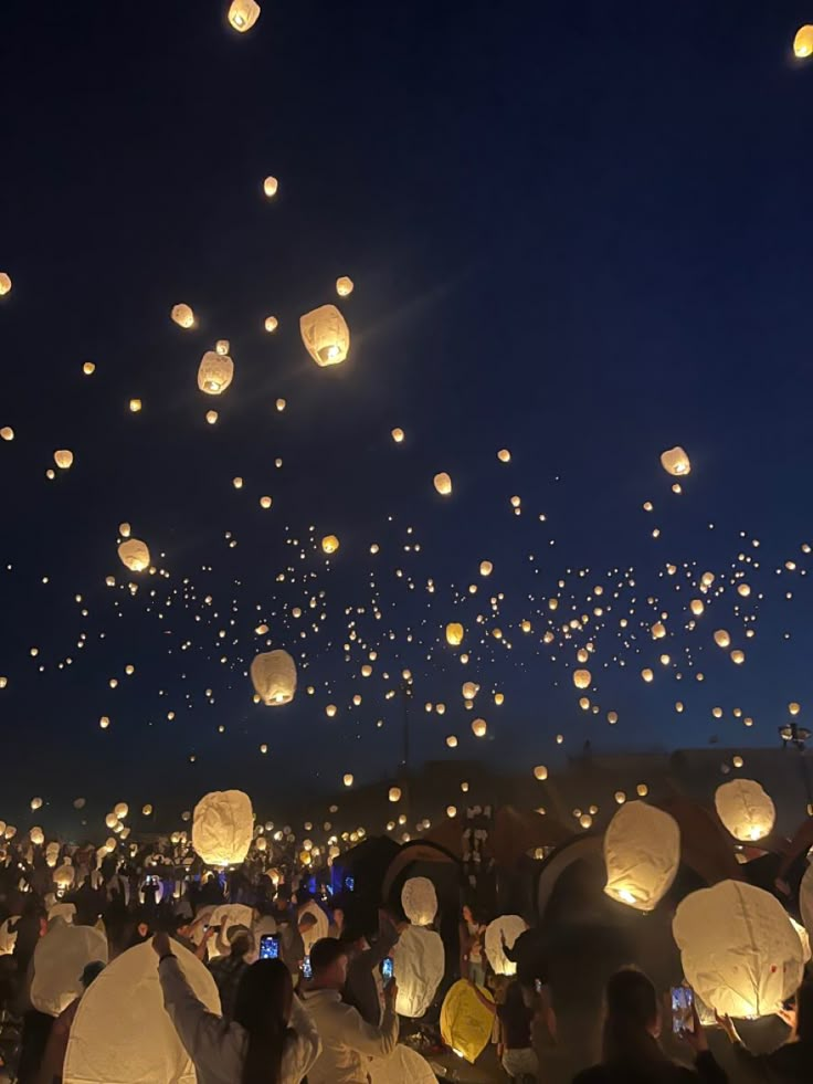 many people are flying paper lanterns in the sky at night with bright lights on them