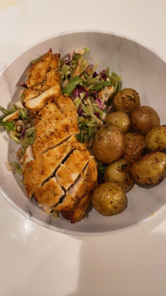 a white plate topped with chicken, potatoes and salad