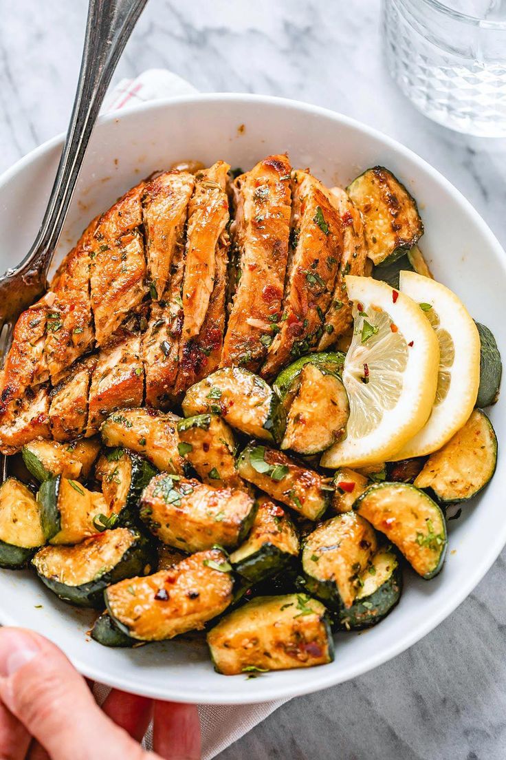 a bowl filled with chicken, zucchini and lemon wedges