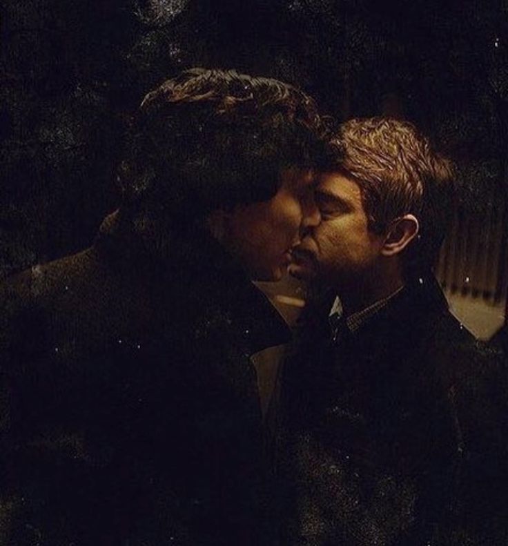 two men standing next to each other with one kissing the other in front of them