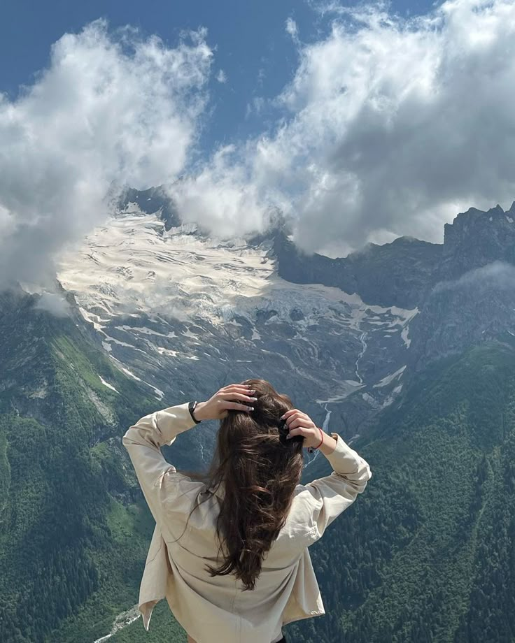 a woman standing on top of a mountain with her hair in the wind and clouds