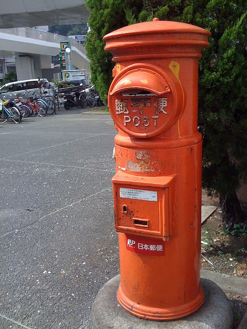 an orange post box sitting on the side of a road next to a parking lot