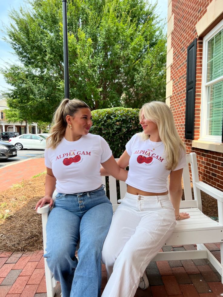 two women sitting on a white bench talking to each other in front of a brick building