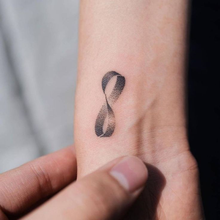 a small tattoo on the wrist of a person's left hand, with an infinite symbol