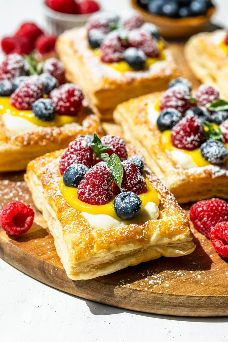 desserts are arranged on a wooden platter with berries and other fruit toppings