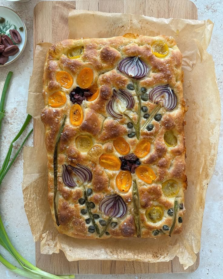 an artisan bread with vegetables on it sitting on a cutting board next to some green onions