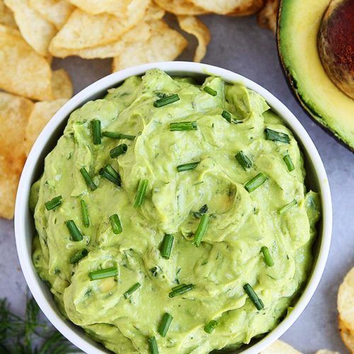 a bowl of guacamole next to chips and an avocado