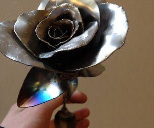 a person holding a metal rose in their hand with the light reflecting off it's petals