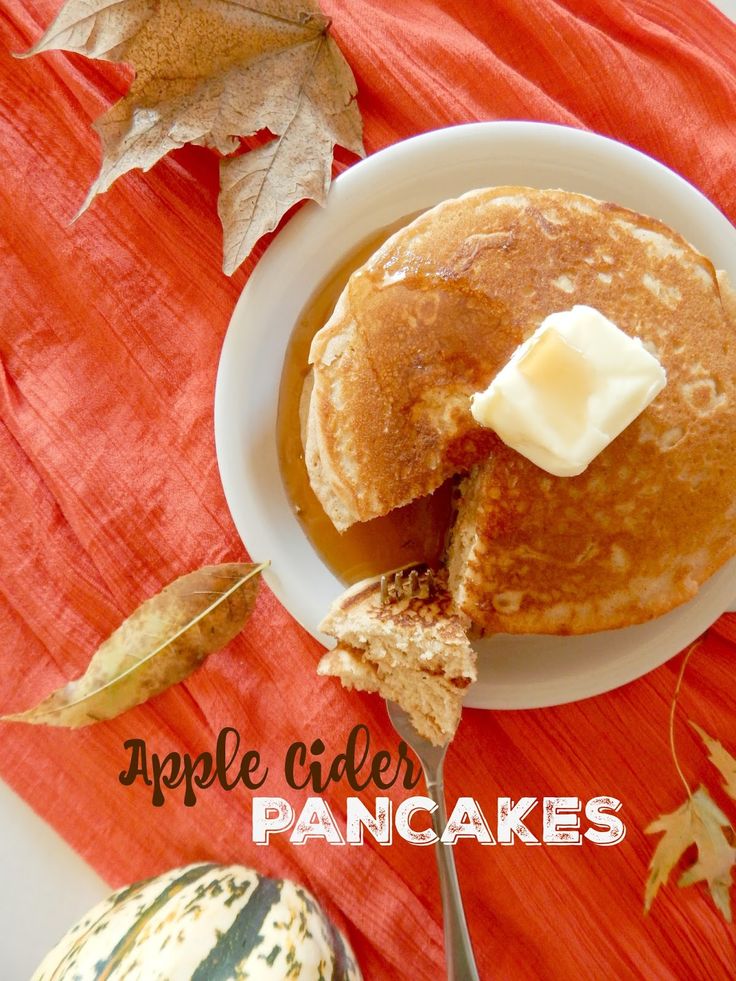 a plate with pancakes and butter on it next to some fall leaves, pumpkins and an apple cider