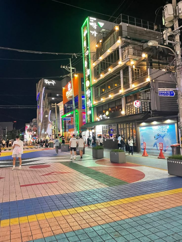 people are walking on the street in front of some buildings at night with neon lights