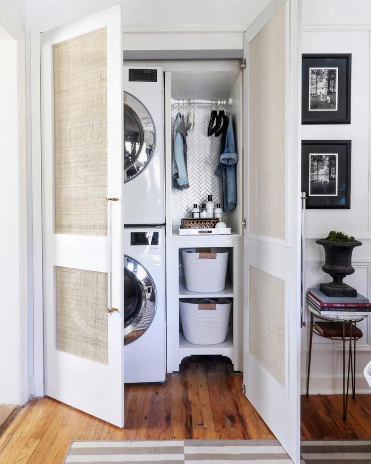 an open closet with clothes hanging on the door and washing machine in it, next to a laundry basket