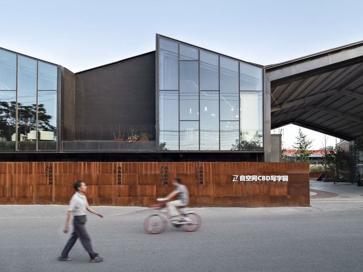 two people riding bikes in front of a building with large windows on the side of it