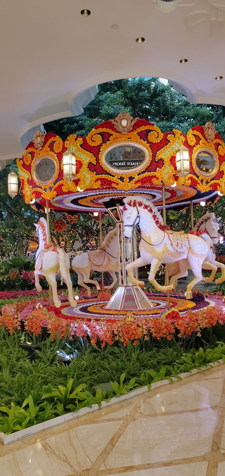 an elaborately decorated merry go round with horses in the center and flowers all around