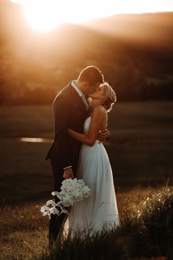 a bride and groom kissing in front of the sun on their wedding day at sunset