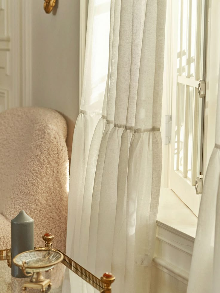 a white chair sitting in front of a window next to a table with a candle on it