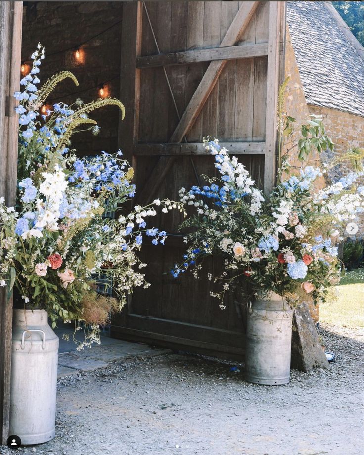 two buckets filled with flowers sitting in front of a barn