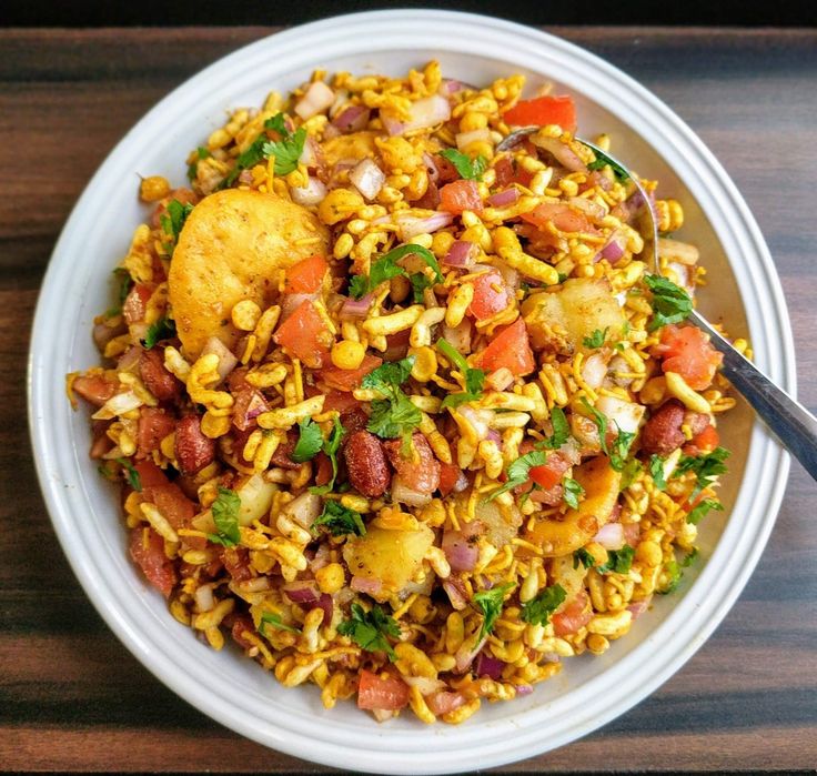 a white bowl filled with rice and vegetables on top of a wooden table next to a fork