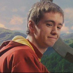 a man holding a large knife in his right hand and smiling at the camera with mountains in the background