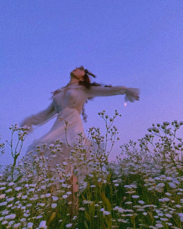 a woman standing in a field of flowers with her arms spread out to the sky