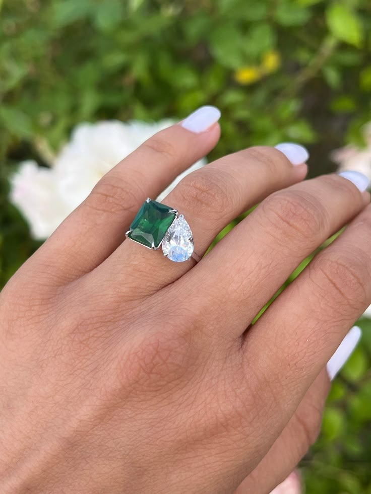 a woman's hand holding a ring with an emerald and white diamond in it