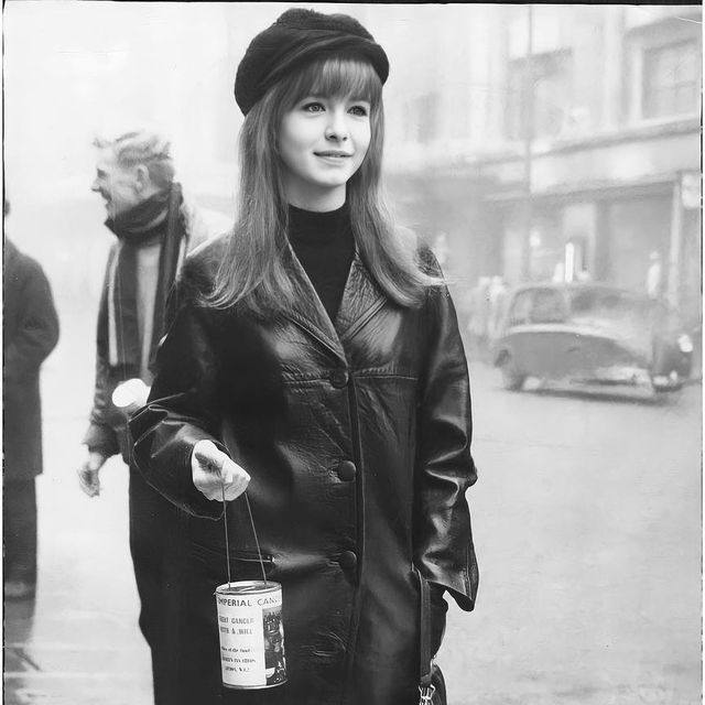 black and white photograph of woman in leather coat holding an empty can on the street