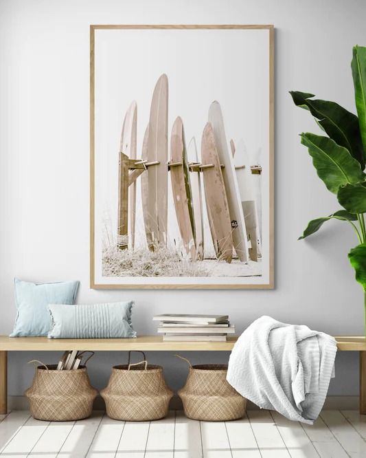 a surfboard art print hangs on the wall above a bench with baskets underneath it