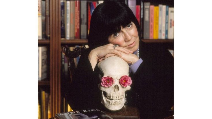 a woman sitting at a table with a skull and roses on her head in front of bookshelves