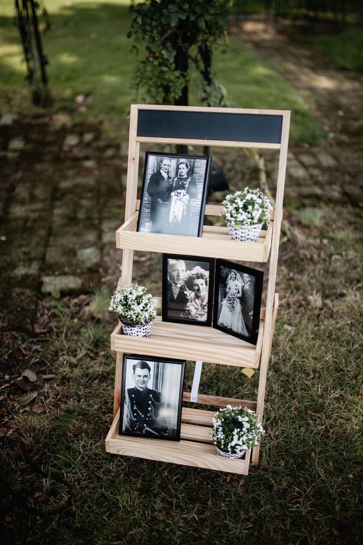 a wooden shelf with pictures and flowers on it in front of some grass, next to a tree