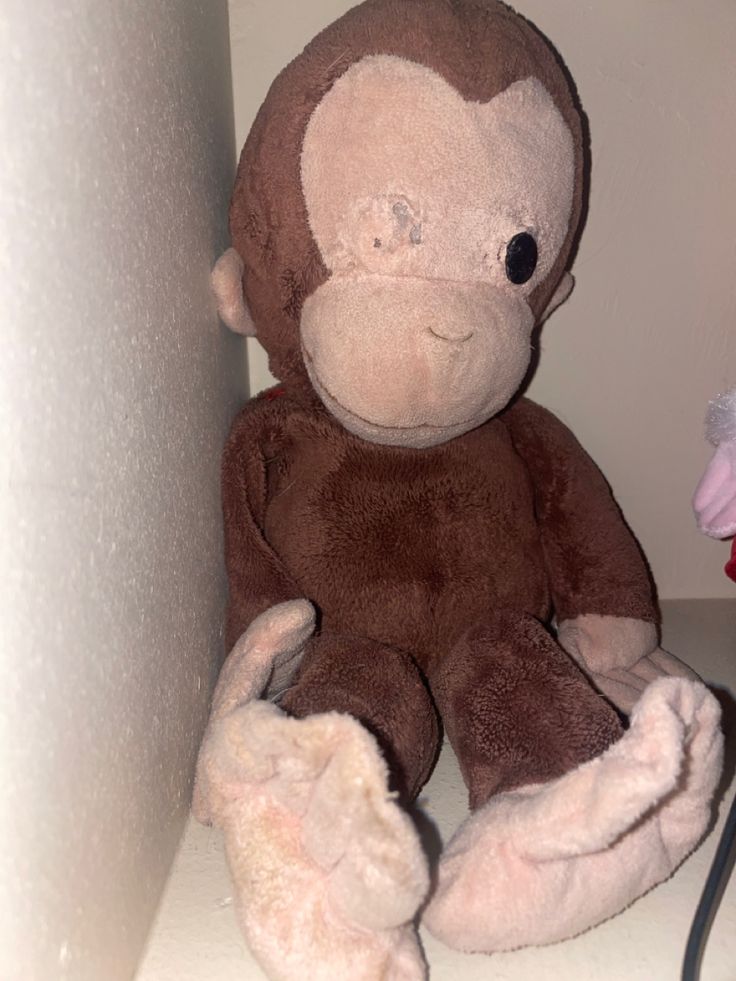 a stuffed monkey sitting on top of a white shelf next to a pink and red flower