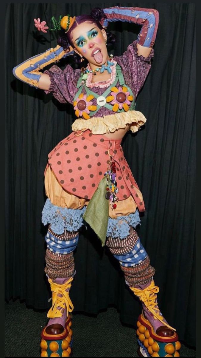 a woman dressed as a clown posing with her hands on her head and legs in the air