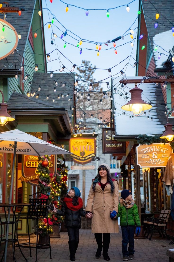 a woman and two children are walking down the street with christmas lights strung over them