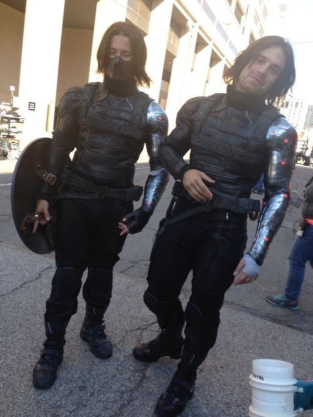 two men dressed in black and silver standing next to each other on a street corner