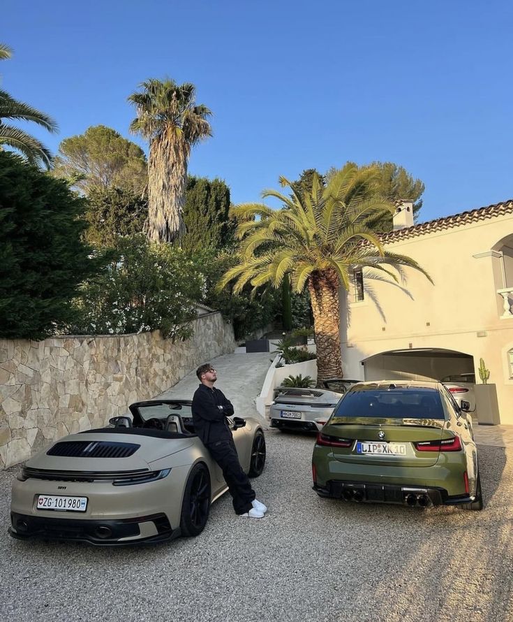 two cars parked next to each other in front of a house with palm trees on the side