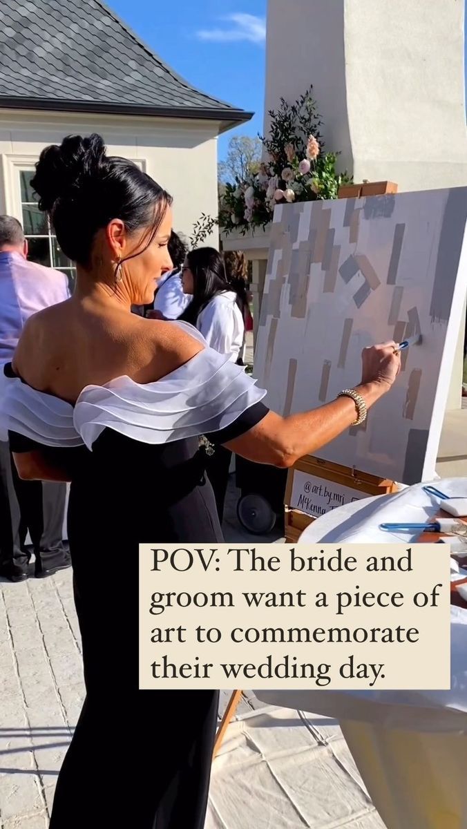 a woman in a black and white dress holding a paintbrush next to an easel