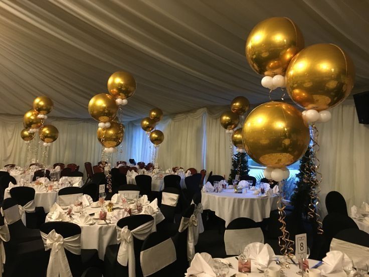 a banquet room set up for a party with gold balloons and white tablecloths